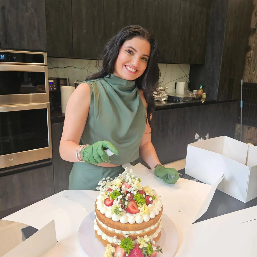 Ari finishing a naked cake decorated with fresh flowers and berries