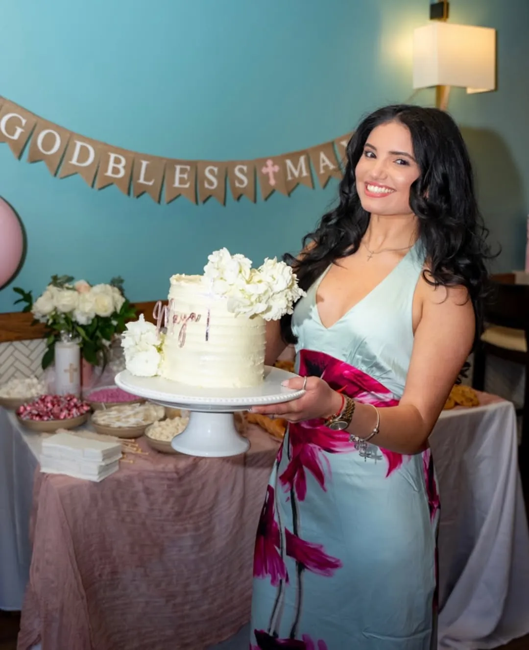 Ari beside a white floral cake on a dessert table for a First Communion