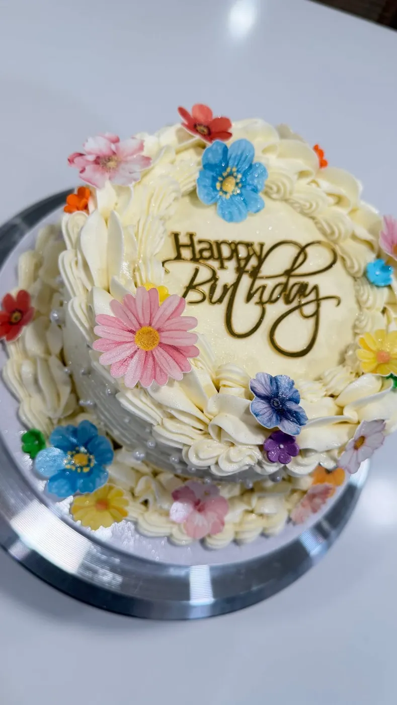Buttercream cake covered in colorful sugar flowers with a gold Happy Birthday topper