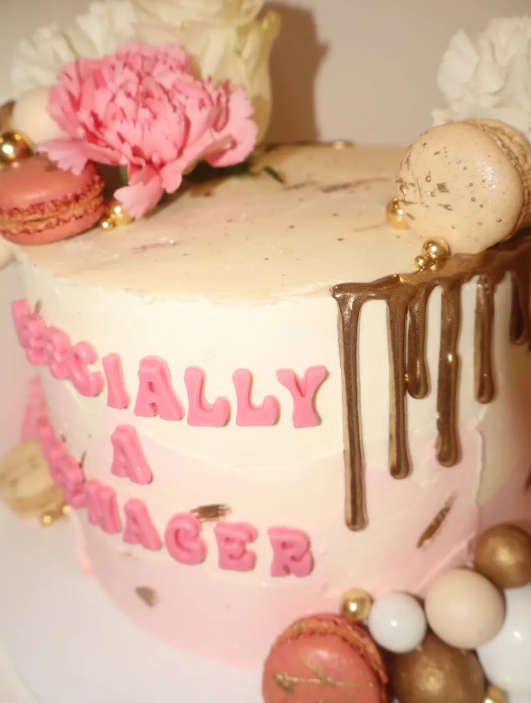 Pink cake with a chocolate drip, macarons and a carnation