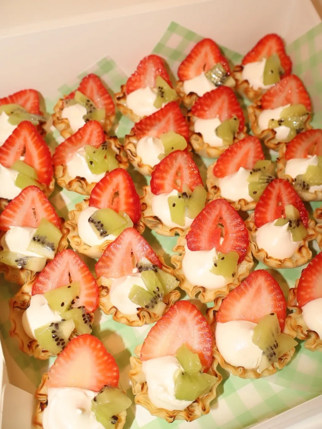 Rows of mini tarts topped with strawberries and kiwi